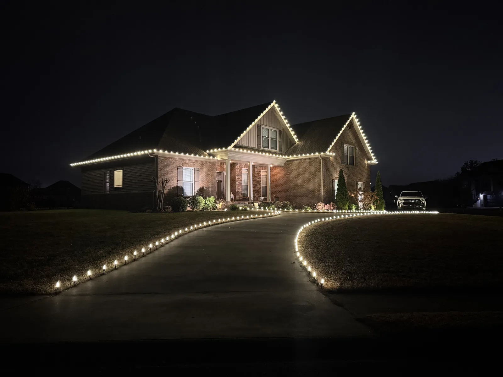 Warm white lights along a home and curving driveway