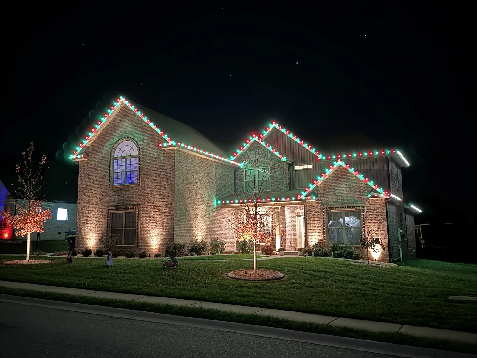 Red and green Christmas lights tracing a brick home’s roofline