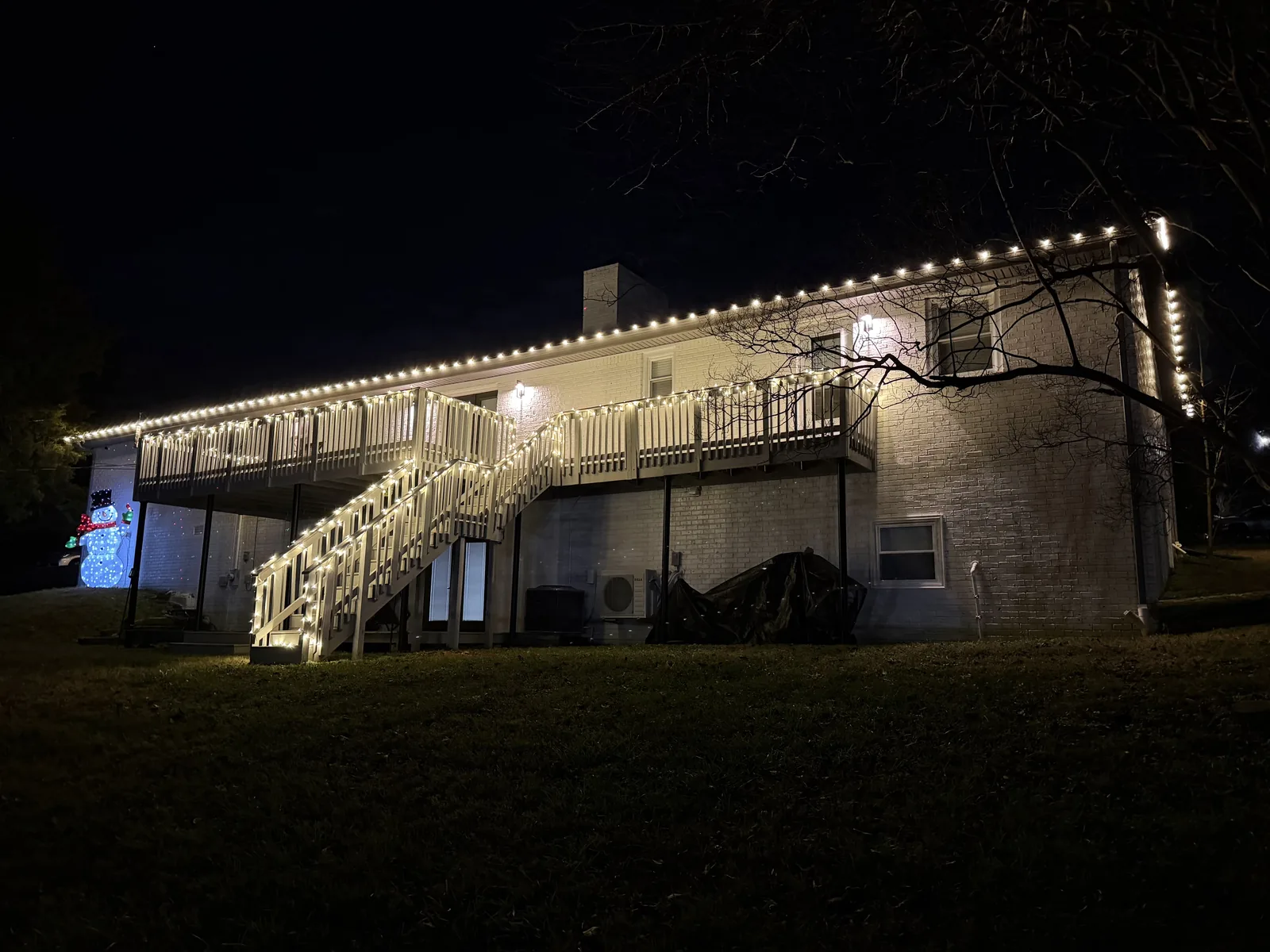 Warm white lights outlining a home’s roofline, deck and exterior stairs